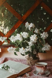 Photo of Bouquet of beautiful jasmine flowers in vase, open book and aromatic tea on fabric indoors