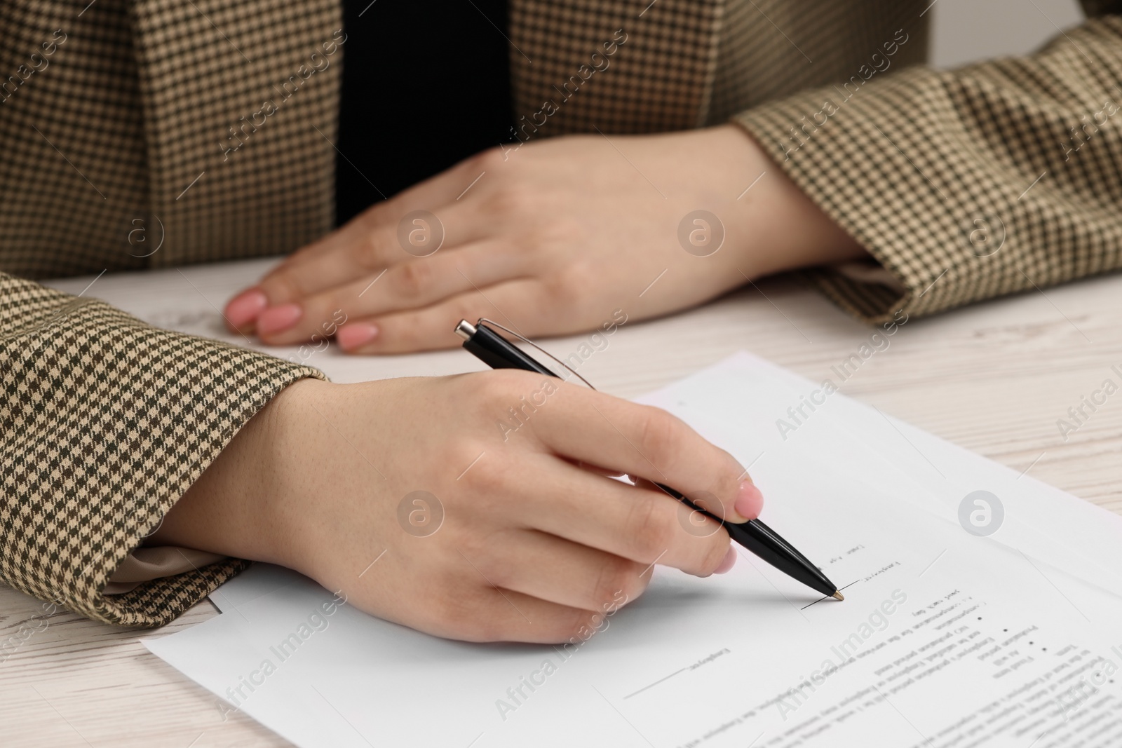 Photo of Woman signing document at wooden table, closeup