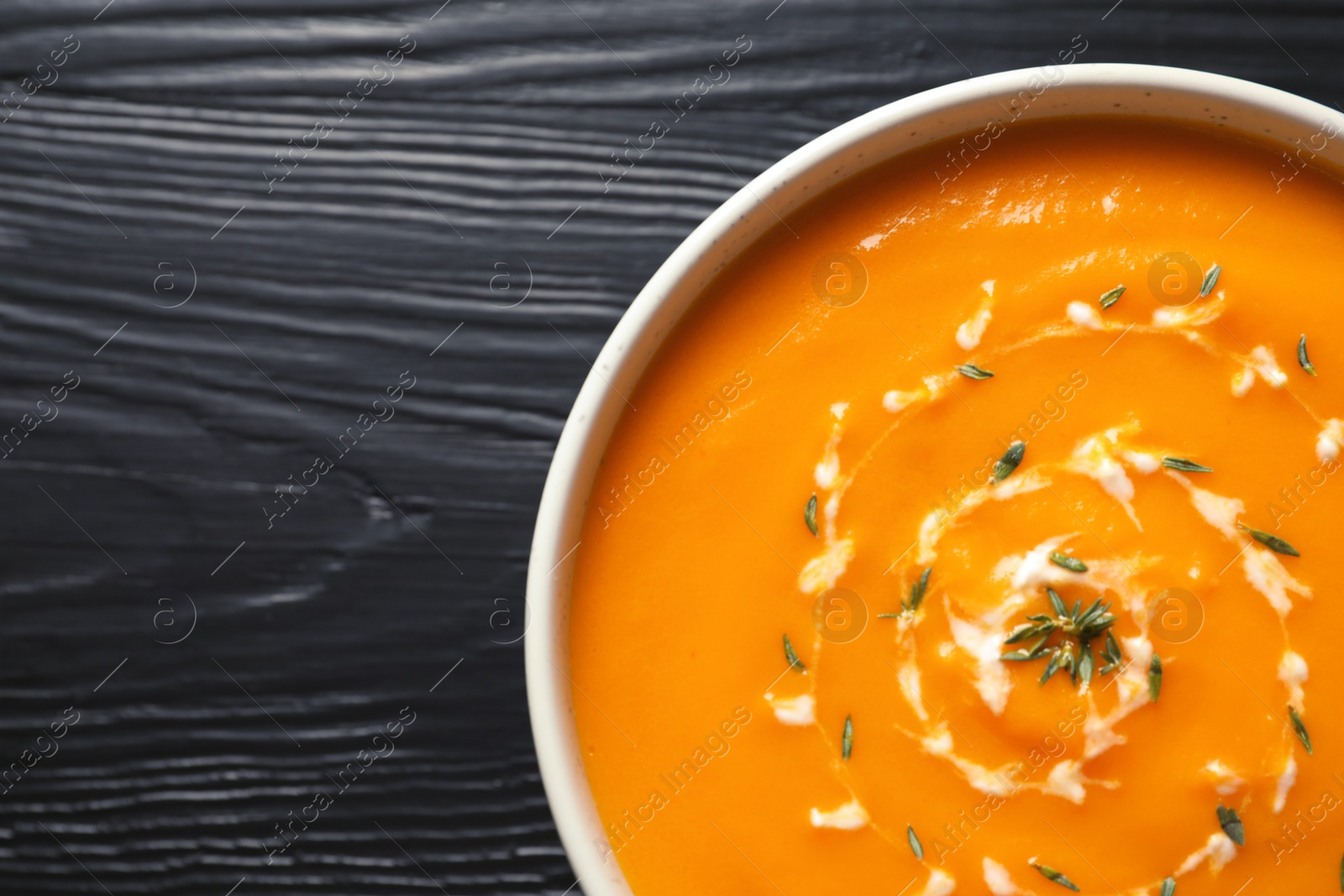 Photo of Delicious pumpkin cream soup in bowl on wooden background, top view. Space for text