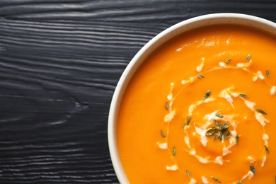 Delicious pumpkin cream soup in bowl on wooden background, top view. Space for text