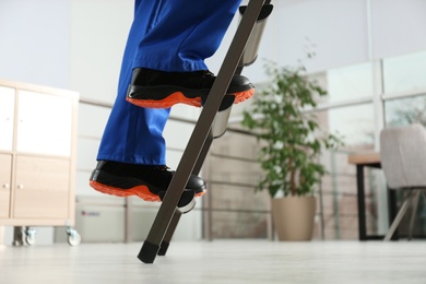 Photo of Professional worker climbing up ladder in room, closeup. Space for text