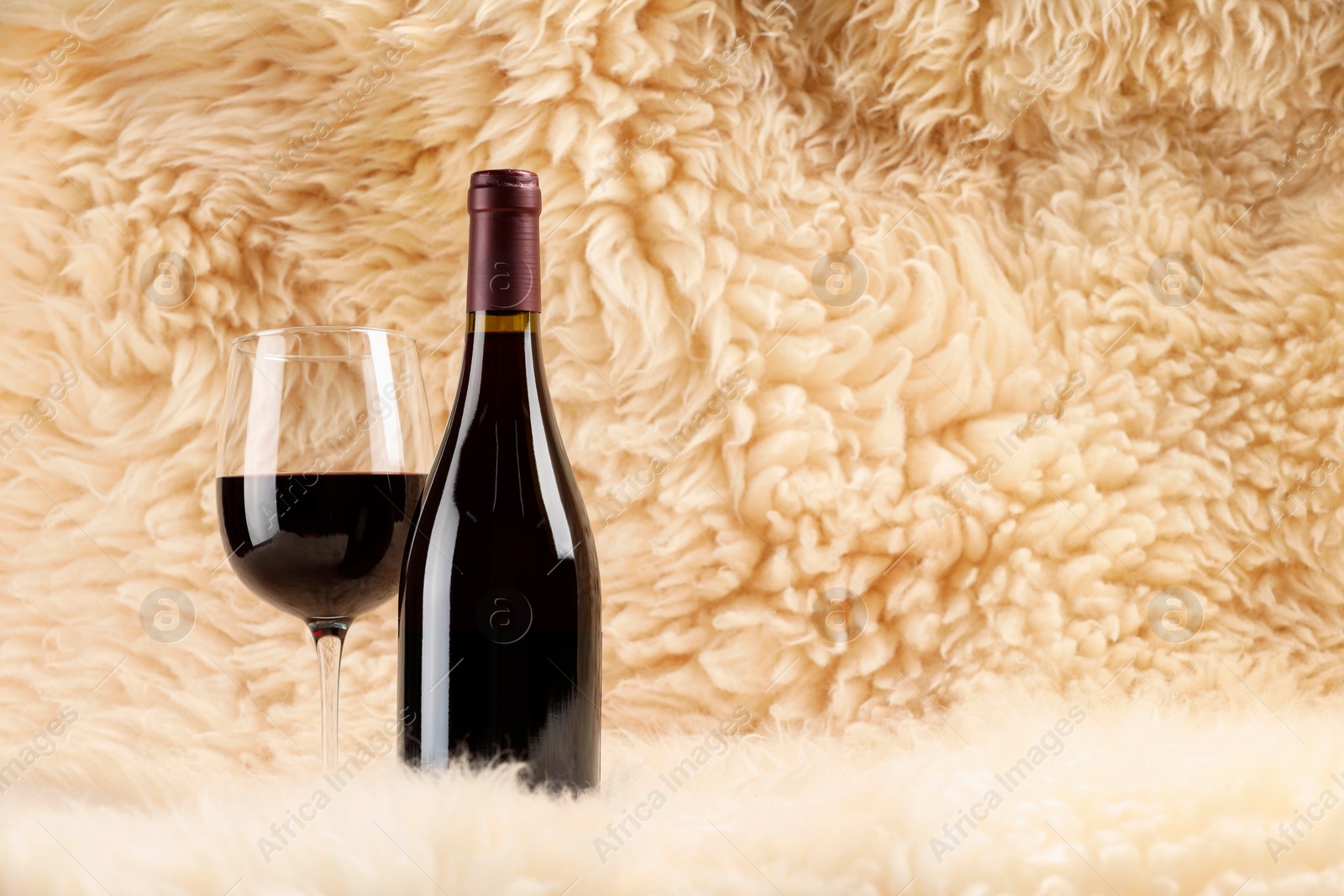 Photo of Stylish presentation of delicious red wine in bottle and glass on fluffy surface. Space for text