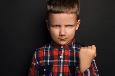 Angry little boy on black background. Aggressive behavior