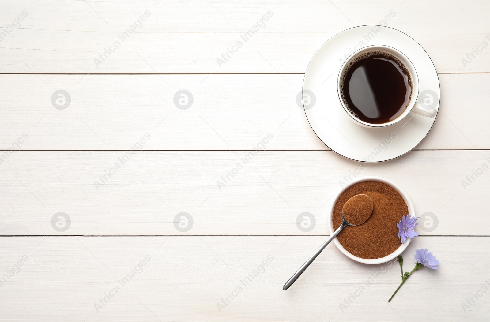 Photo of Cup of delicious chicory drink, powder and flowers on white wooden table, flat lay. Space for text