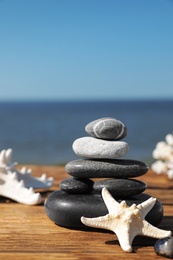 Photo of Stack of stones and starfishes on wooden pier near sea, space for text Zen concept