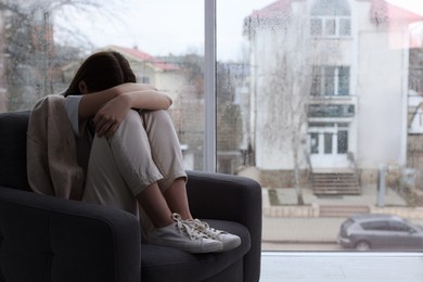Photo of Sad young woman crying near window indoors, space for text. Loneliness concept