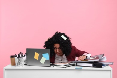 Photo of Stressful deadline. Tired woman looking at laptop at white desk on pink background, space for text. Many sticky notes everywhere as reminders