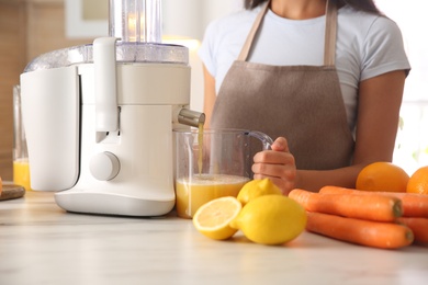Young woman making tasty fresh juice at table in kitchen, closeup