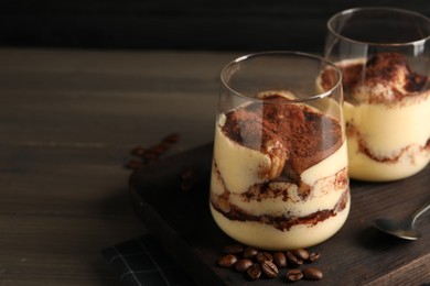 Delicious tiramisu in glasses, spoon and coffee beans on wooden table, closeup. Space for text