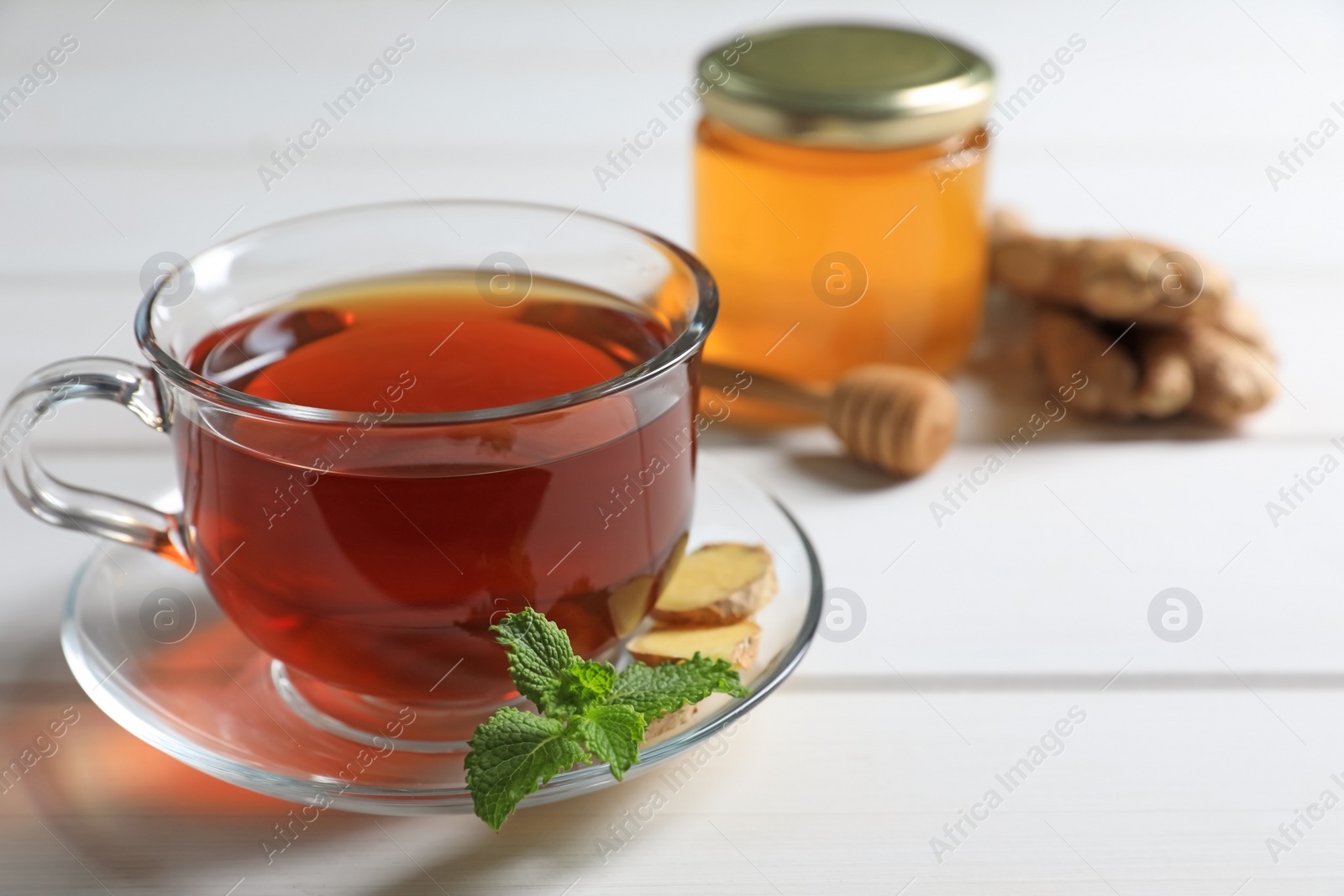 Photo of Cup of delicious ginger tea and ingredients on white wooden table, closeup. Space for text