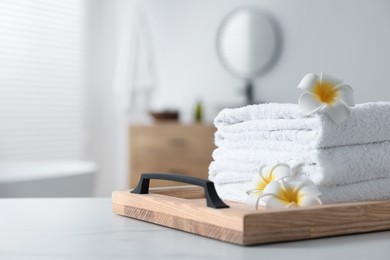 Photo of Wooden tray with stacked bath towels and beautiful flowers on white table in bathroom. Space for text