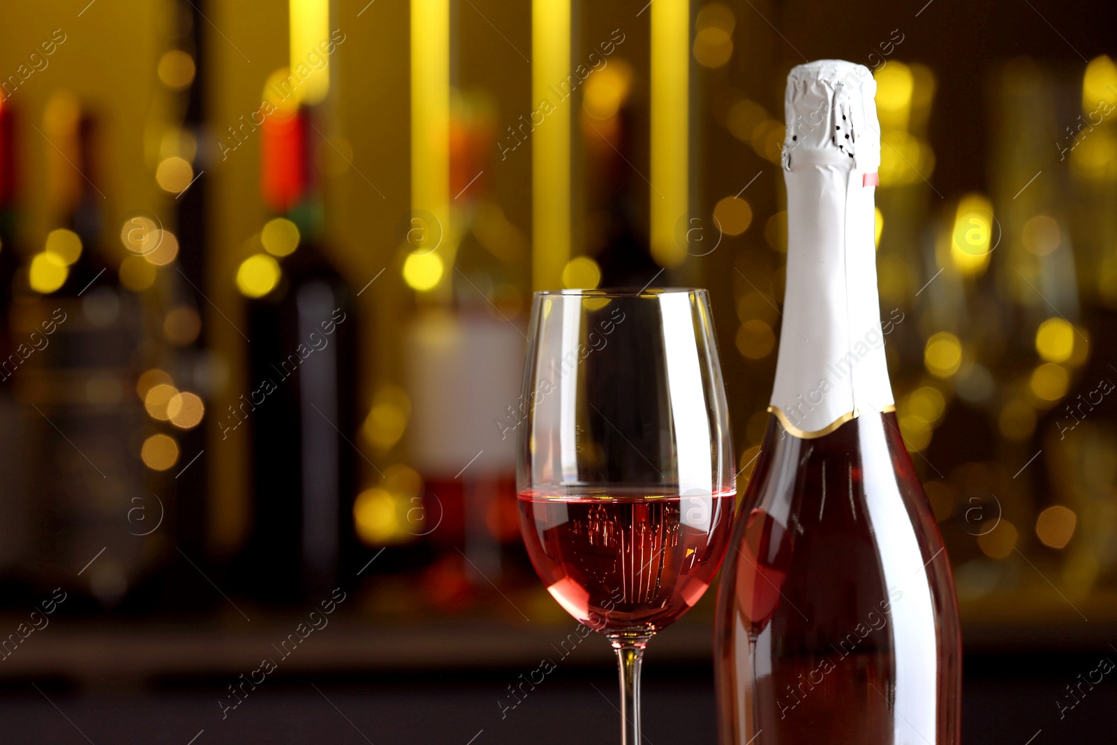 Photo of Bottle and glass of delicious rose wine on blurred background, closeup. Space for text