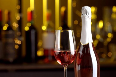 Bottle and glass of delicious rose wine on blurred background, closeup. Space for text