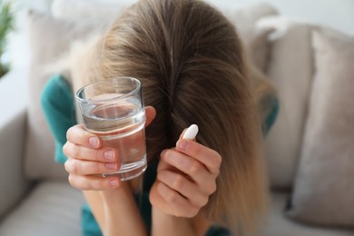 Photo of Upset young woman with abortion pill and glass of water at home, focus on hands