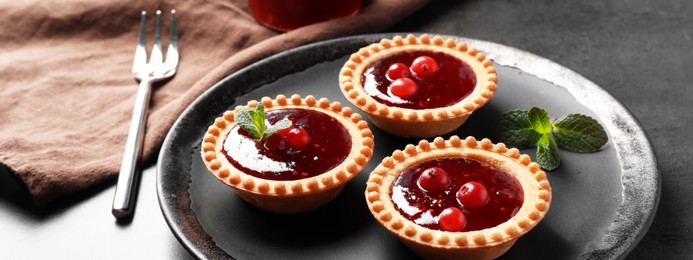 Image of Tasty tartlets with jam on grey table. Banner design