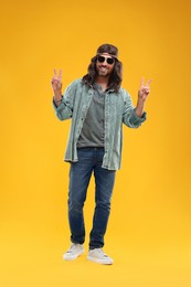 Photo of Stylish hippie man in sunglasses showing V-sign on orange background