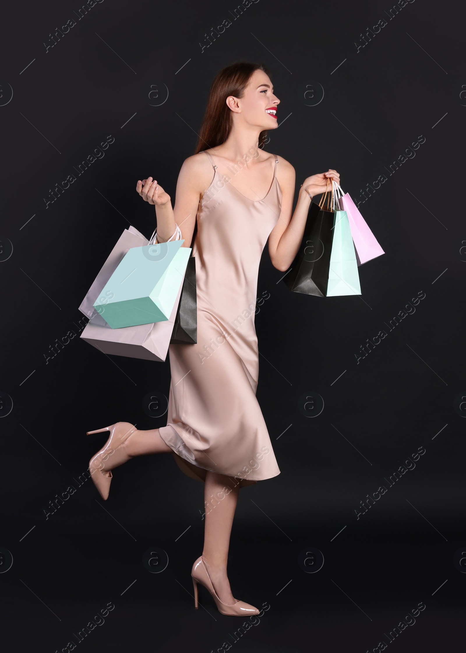 Photo of Happy young woman with shopping bags on black background. Big sale