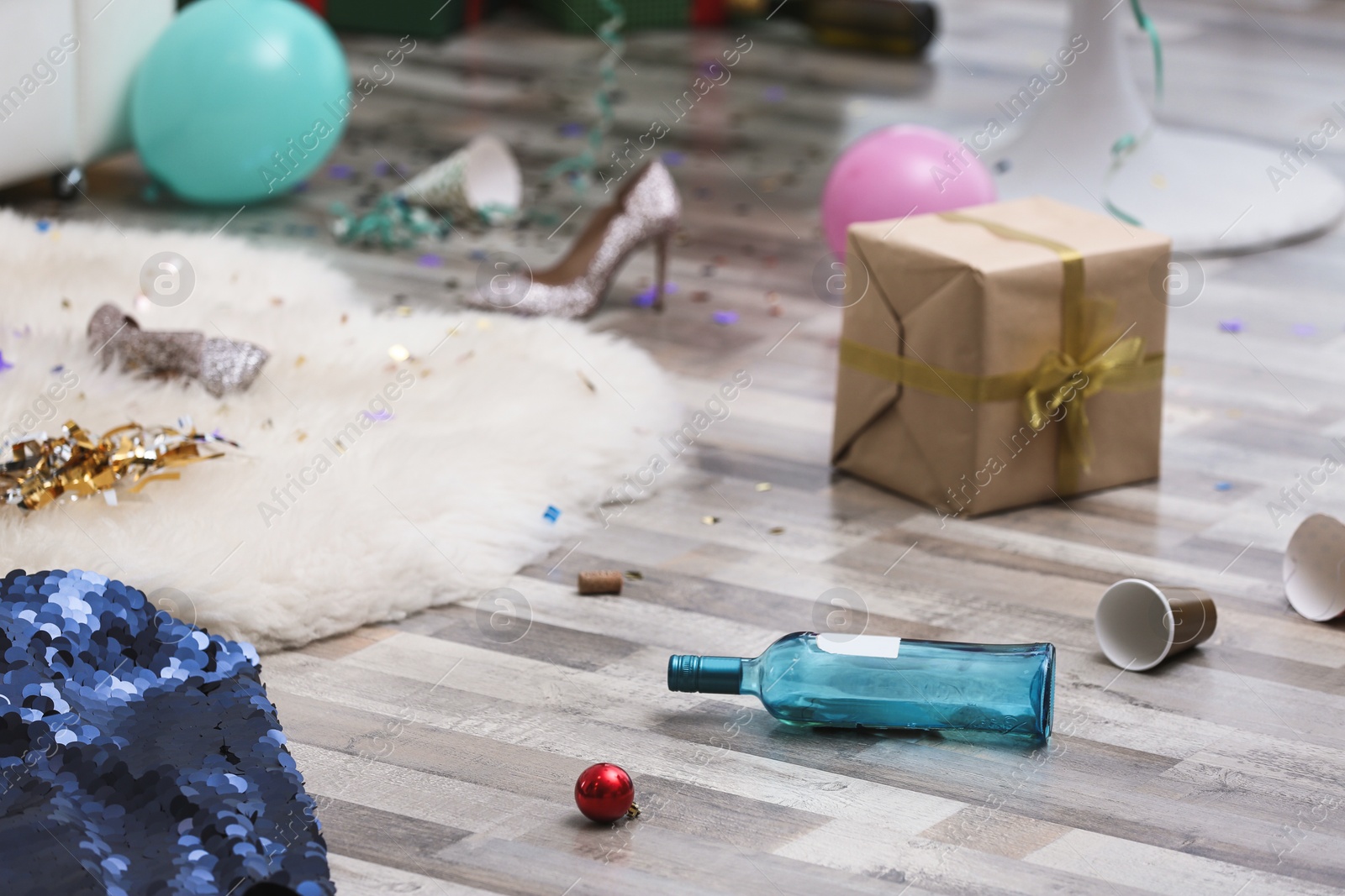 Photo of Empty bottle, dress and gift box on messy floor. Chaos after party