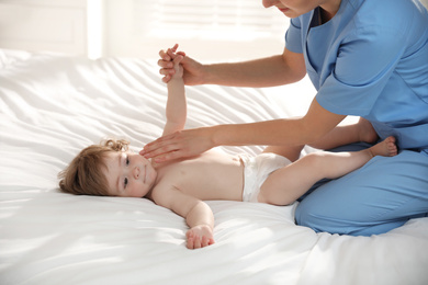 Photo of Orthopedist examining cute little baby on bed