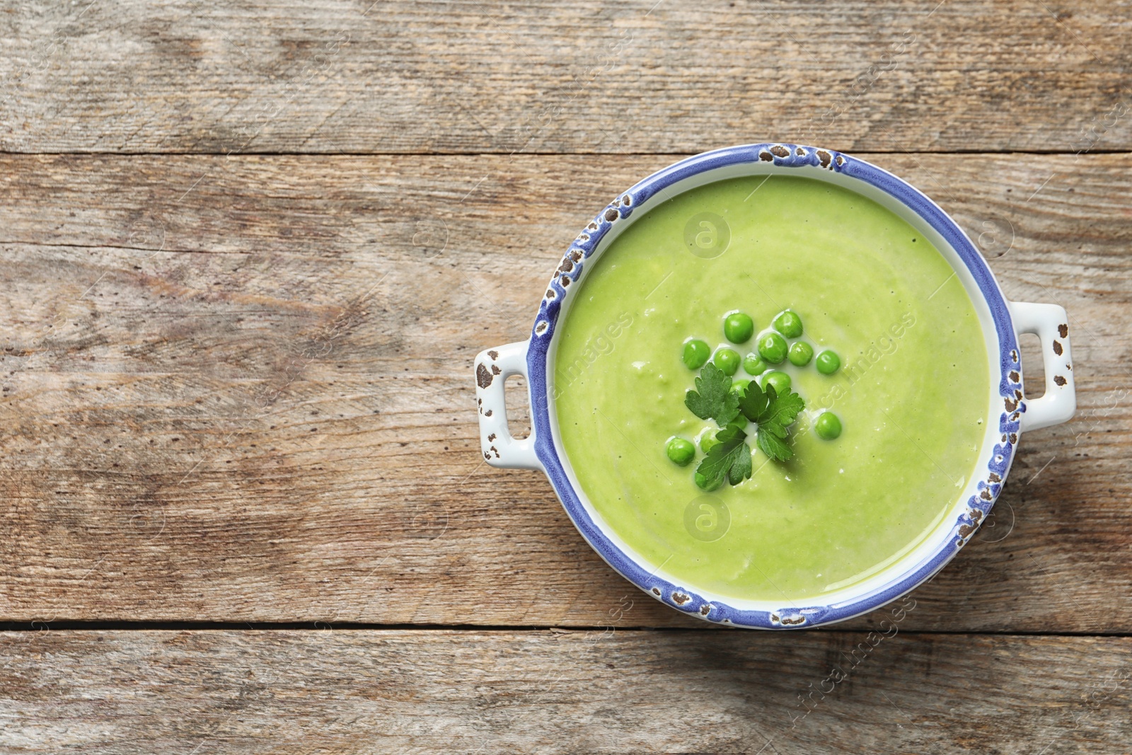 Photo of Fresh vegetable detox soup made of green peas in dish and space for text on wooden background, top view