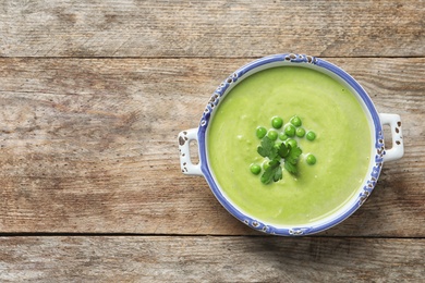 Photo of Fresh vegetable detox soup made of green peas in dish and space for text on wooden background, top view
