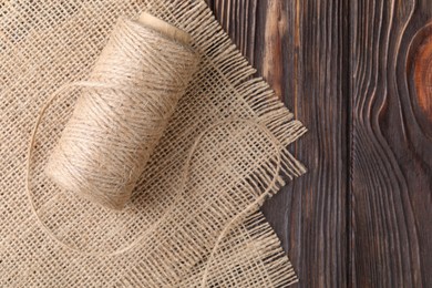 Photo of Spool of thread and burlap fabric on wooden table, top view. Space for text