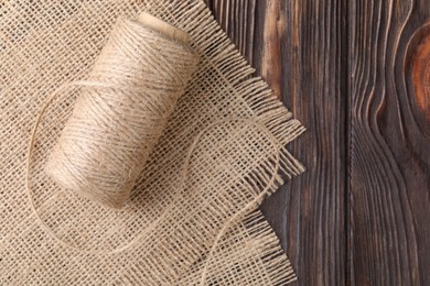 Spool of thread and burlap fabric on wooden table, top view. Space for text