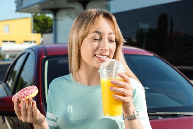 Photo of Beautiful young woman with doughnut drinking juice near car at gas station