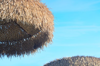 Photo of Beautiful straw beach umbrella against blue sky, closeup. Space for text