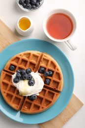 Tasty Belgian waffle with blueberries, honey and whipped cream served on white table, flat lay