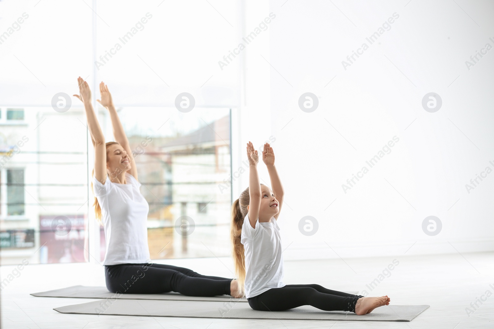 Photo of Mother and daughter in matching sportswear doing yoga together at home