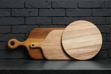 Photo of Different wooden cutting boards on gray table near dark brick wall