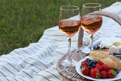 Glasses of delicious rose wine, food and basket on picnic blanket outdoors