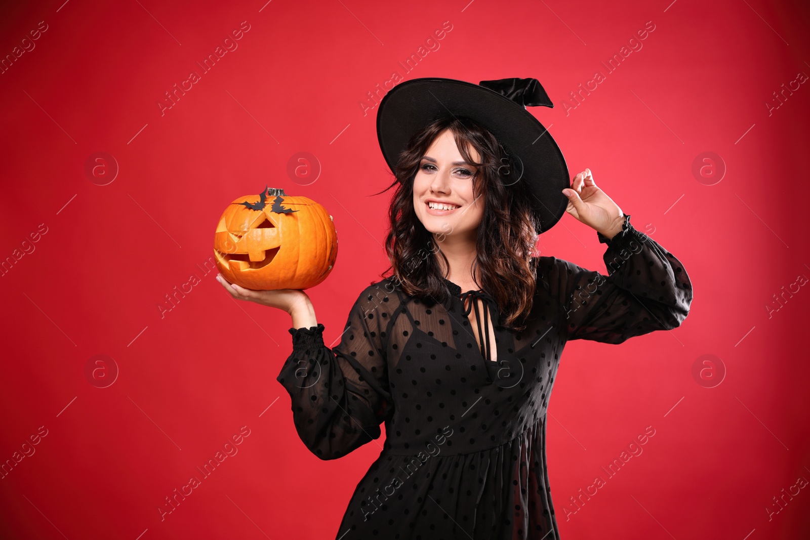 Photo of Beautiful woman in witch costume with jack o'lantern on red background. Halloween party