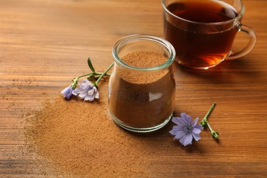 Jar with chicory powder, cup of delicious drink and flowers on wooden table