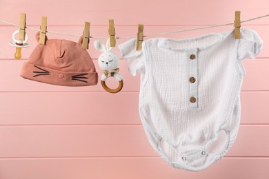 Photo of Baby clothes and accessories hanging on washing line near pink wooden wall