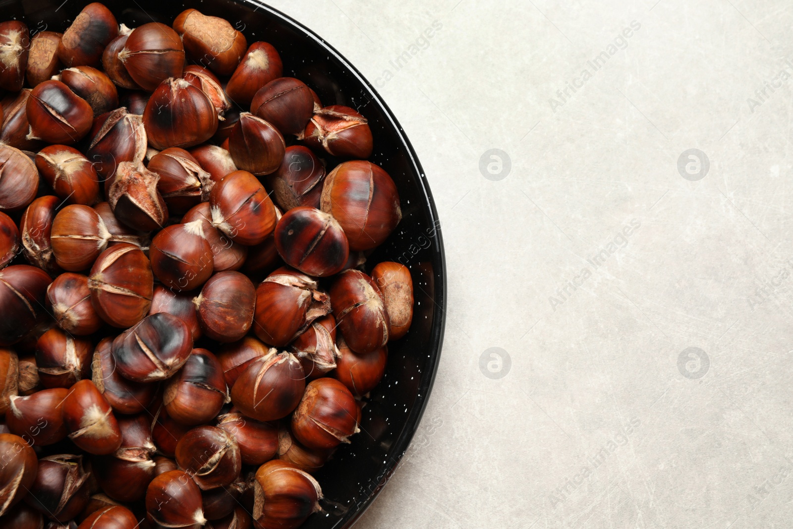 Photo of Delicious roasted edible chestnuts on light grey table, top view. Space for text
