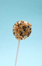 Photo of Sweet cake pop decorated with sprinkles on light blue background, closeup. Delicious confectionery