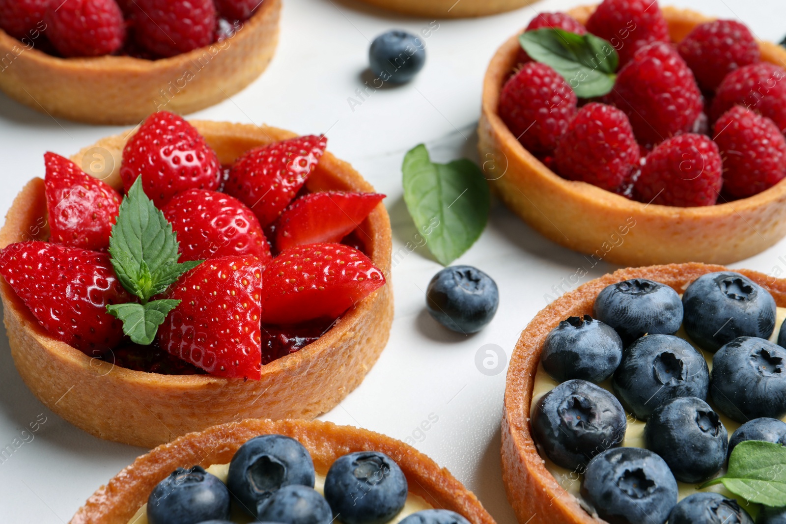 Photo of Tartlets with different fresh berries on white table, closeup. Delicious dessert