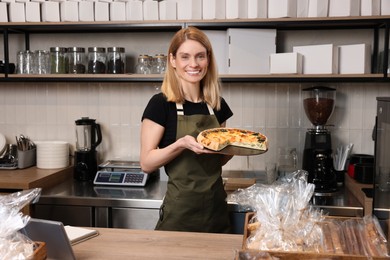 Photo of Happy seller holding delicious quiche at cashier desk in bakery shop