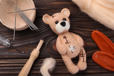 Photo of Felted bear, wool and tools on wooden table, flat lay