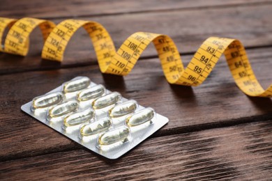 Photo of Oil capsules and measuring tape on wooden table. Weight loss