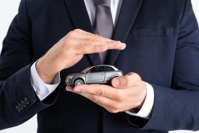 Male insurance agent holding toy car on white background, closeup