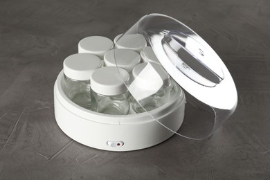 Modern yogurt maker with empty jars on grey table