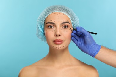 Photo of Doctor with pencil preparing patient for cosmetic surgery operation on light blue background