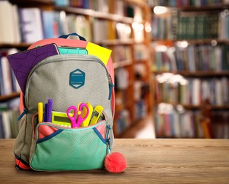 Backpack with school stationery on wooden table in library, space for text