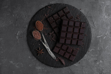 Photo of Tasty dark chocolate and spoons with cocoa powder on grey table, top view