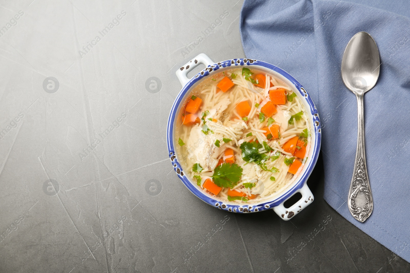 Photo of Homemade chicken soup served on grey table, top view with space for text