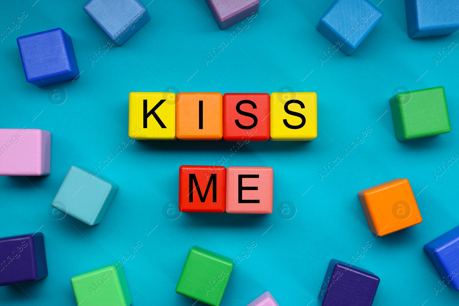 Photo of Colorful cubes with phrase Kiss Me on light blue background, flat lay