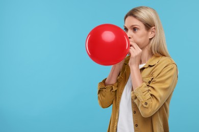 Woman blowing up balloon on light blue background. Space for text